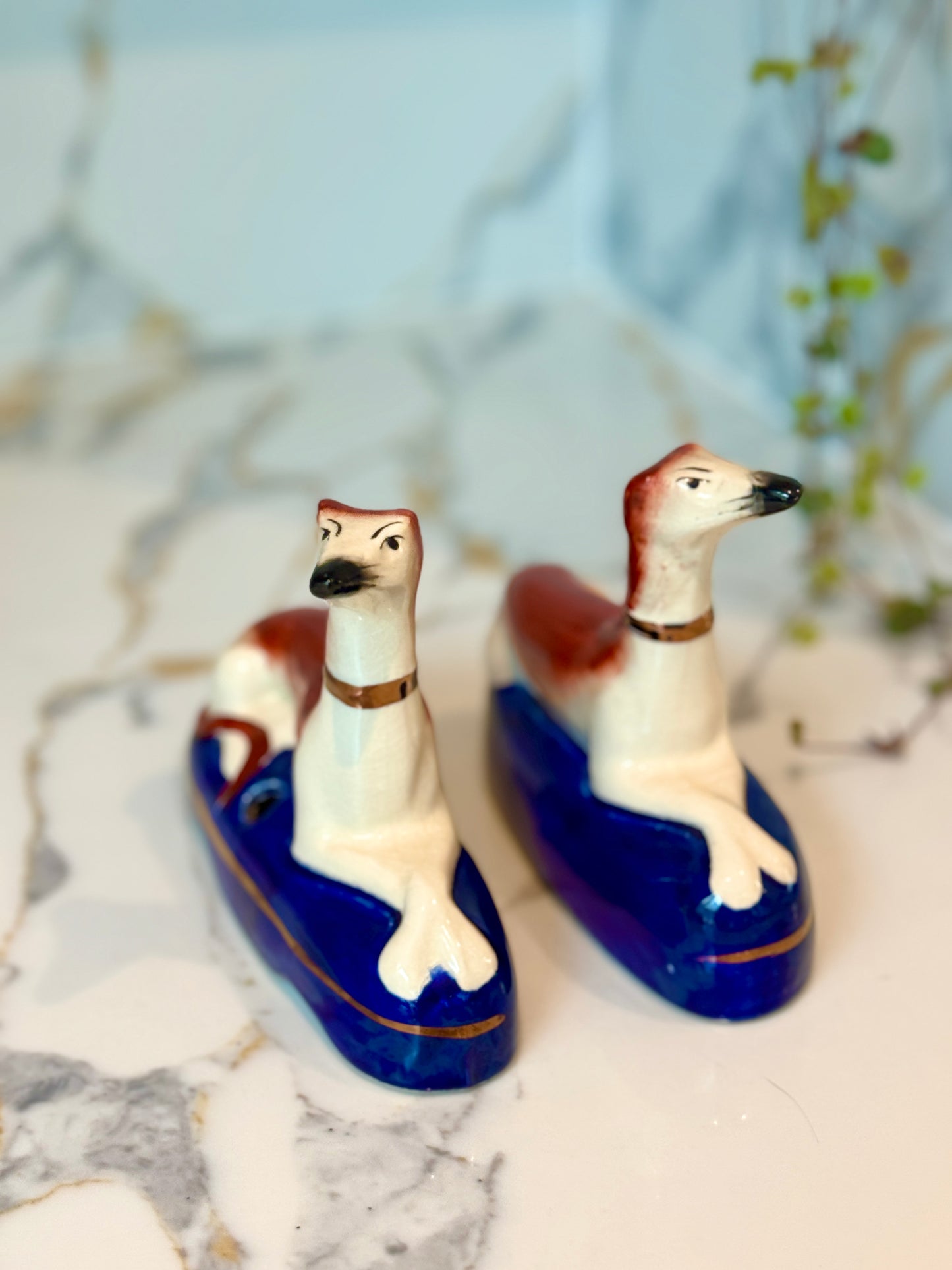Two ceramic dog figurines on blue bases with a marble background