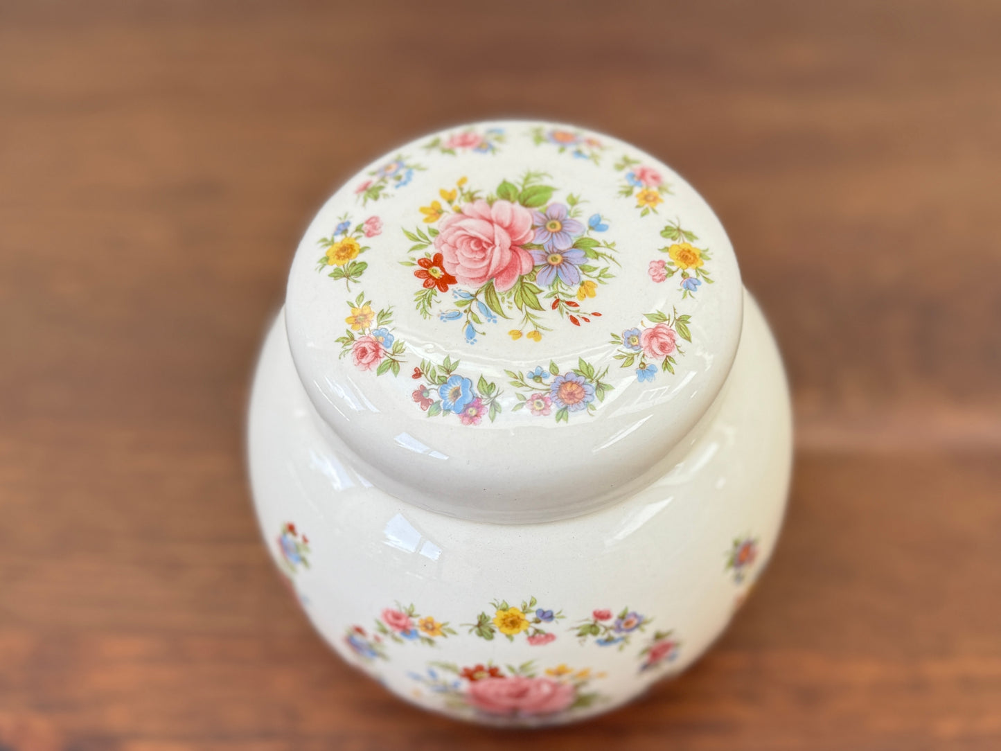 White ceramic jar with floral lid on a wooden surface