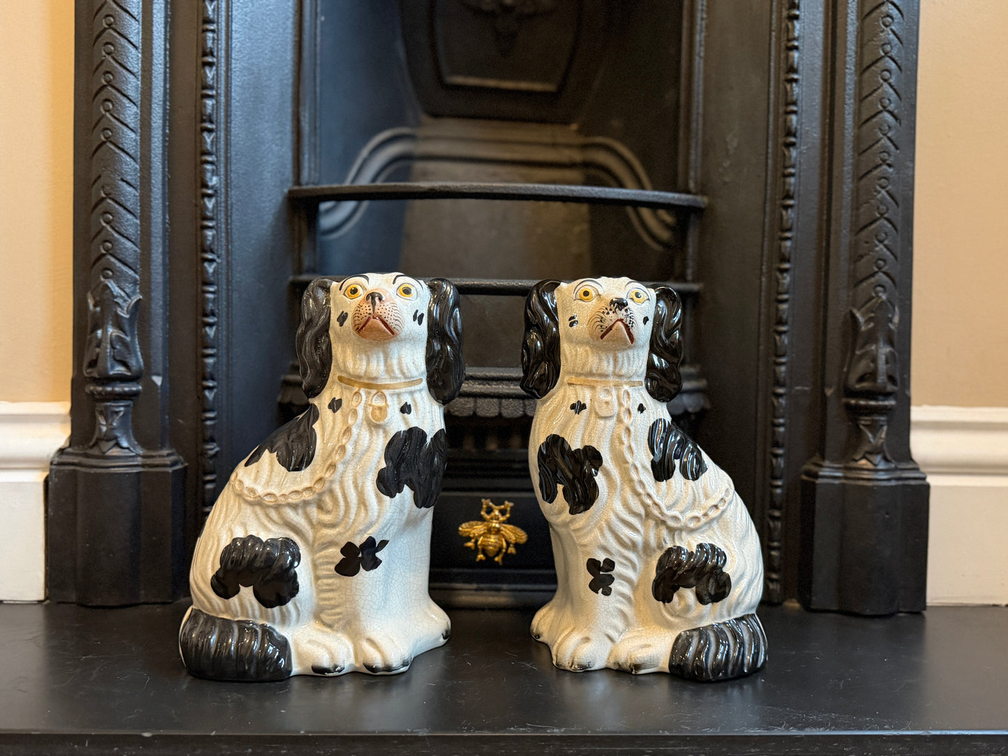 Two ceramic dog figurines on a fireplace mantel with a decorative black frame.
