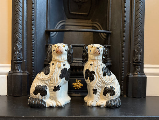 Two ceramic dog figurines on a fireplace mantel with a decorative black frame.