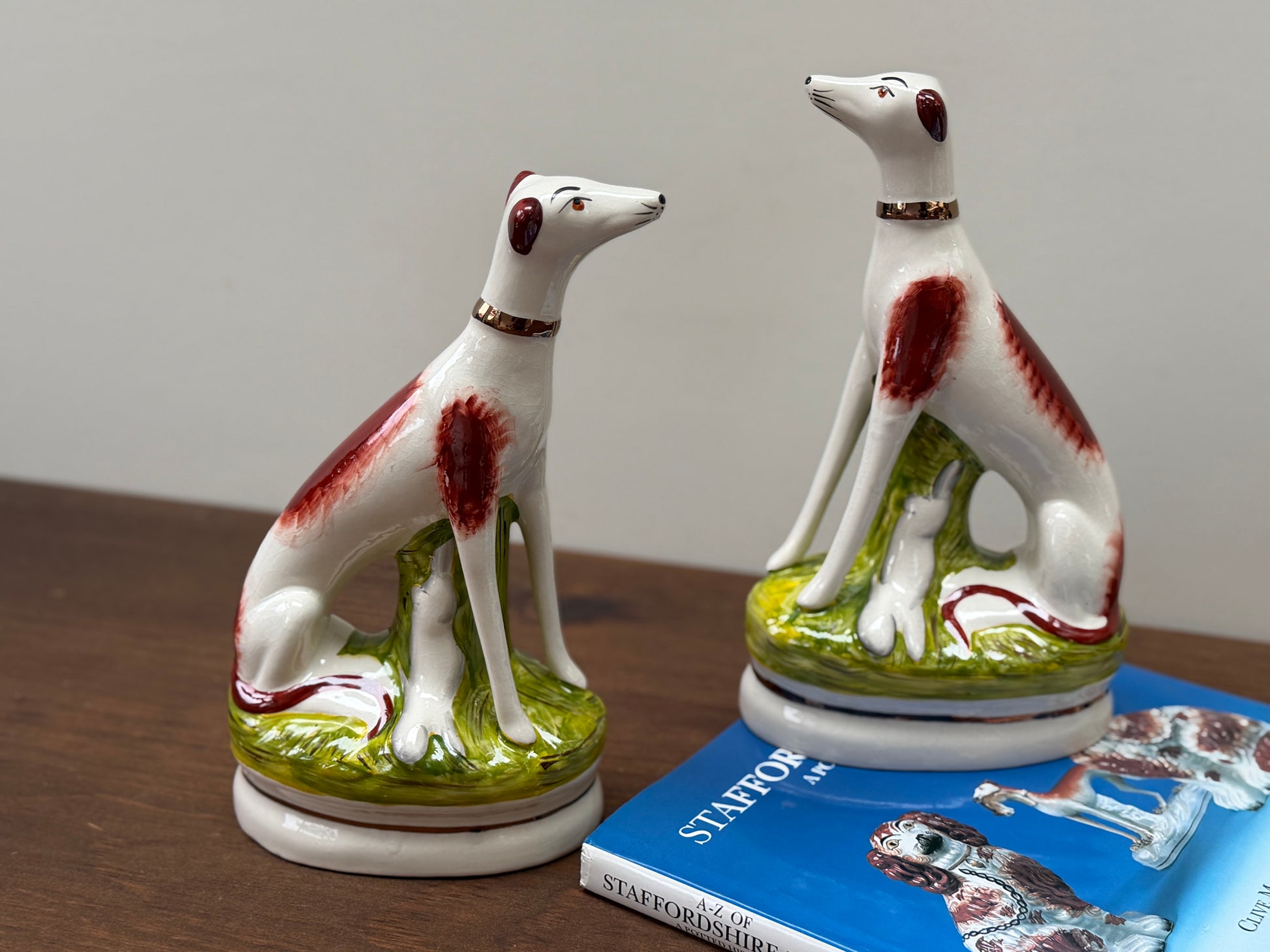 Two ceramic dog figurines on a wooden surface with a book in the background.