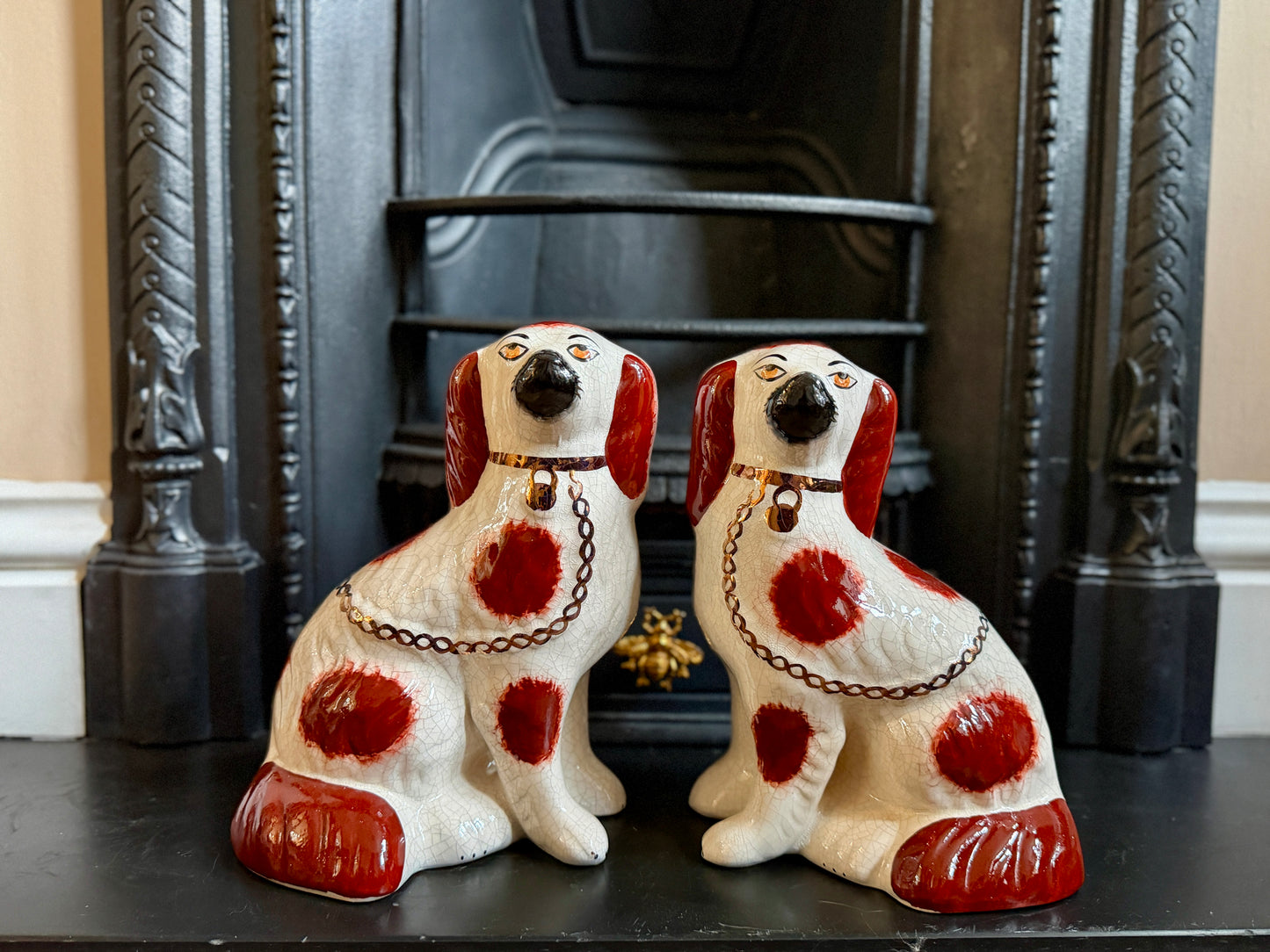 Two ceramic dog figurines with red spots on a mantelpiece.