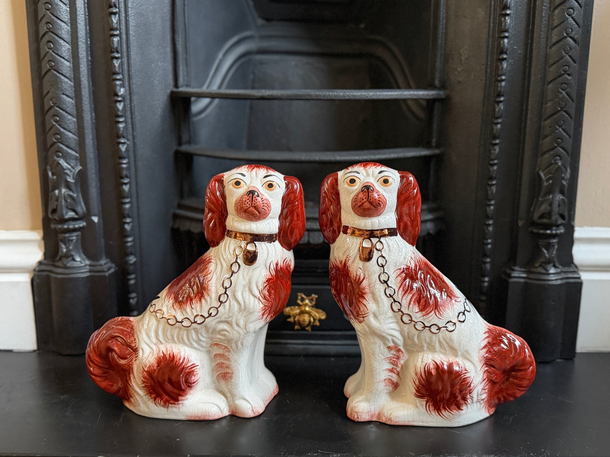 Two ceramic dog figurines with red and white patterns in front of a black fireplace.