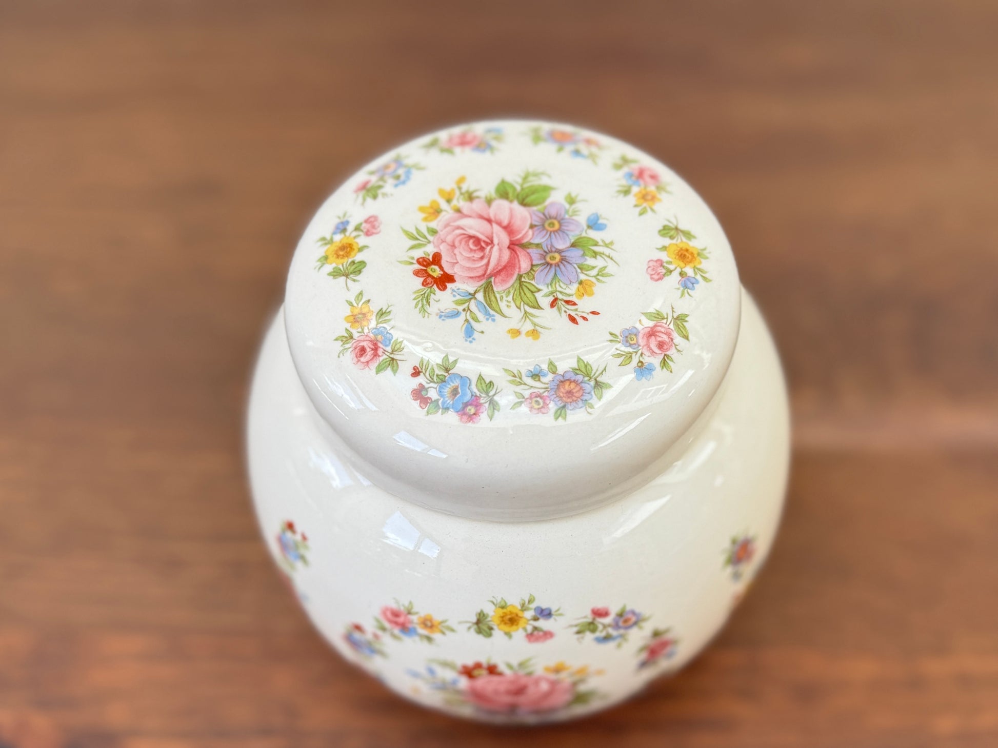 White ceramic jar with floral lid on a wooden surface